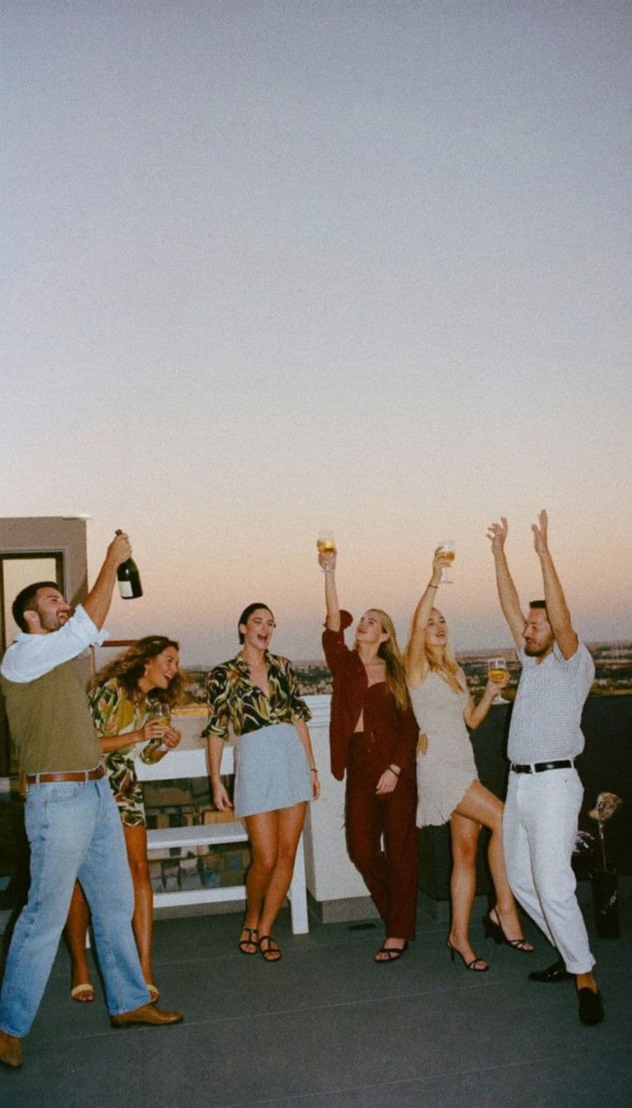 Friends raising their glasses on a rooftop at sunset