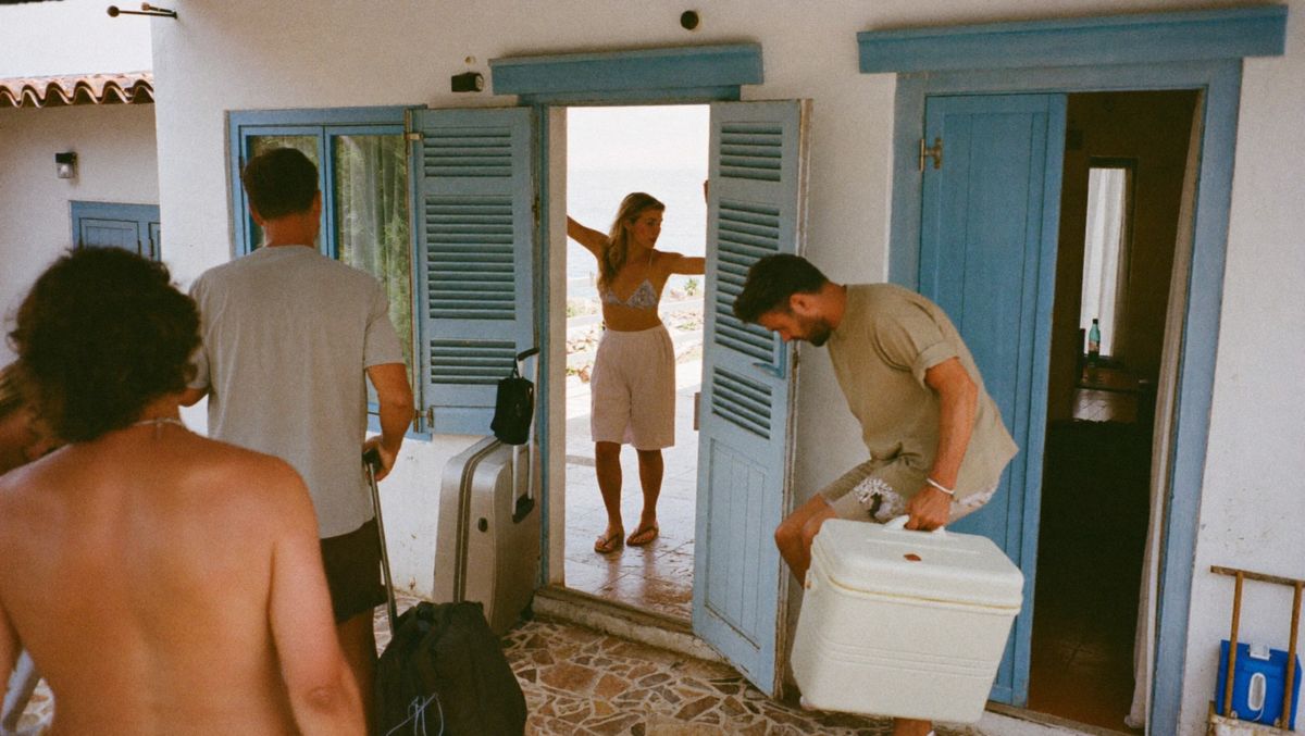 Friends carrying bags through the blue doors of a whitewashed house